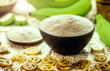 Ev yapımı yeşil muz unu, arka planda meyve ve kızarmış muz cipsi ve dilimler var.