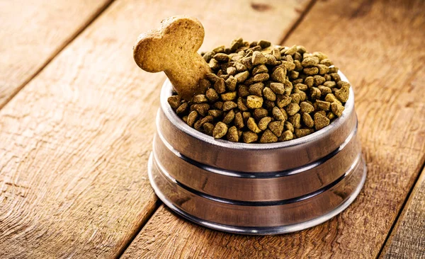 dog food with bone shaped dog biscuit in metallic bowl on wooden background, copy space