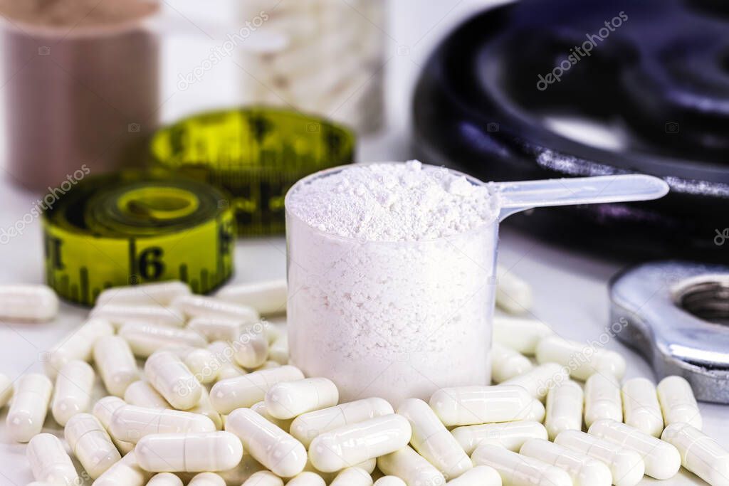 Measuring spoons of dietary supplement, various flavored whey and creatine pills, with weights in the background