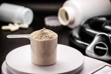 Measuring spoon with creatine or whey, on precision scale, preparing food supplement or casein cocktail, muscle mass vitamin