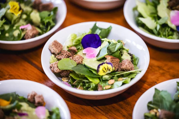 vegetable salad, vegetables and flowers. multiple salad bowls with arugula, flower petals, vegan toast