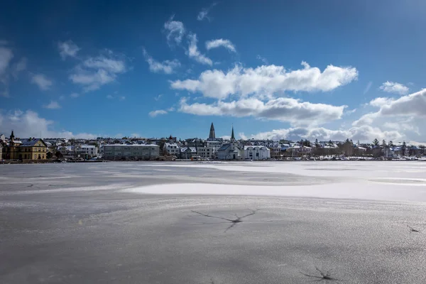Reykjavik, İzlanda - 8 Nisan 2021: Donmuş bir Tjorninn Gölü 'nün yüzeyinden görünen bir şehir manzarası. Güneşli kış günü, insan yok.. 