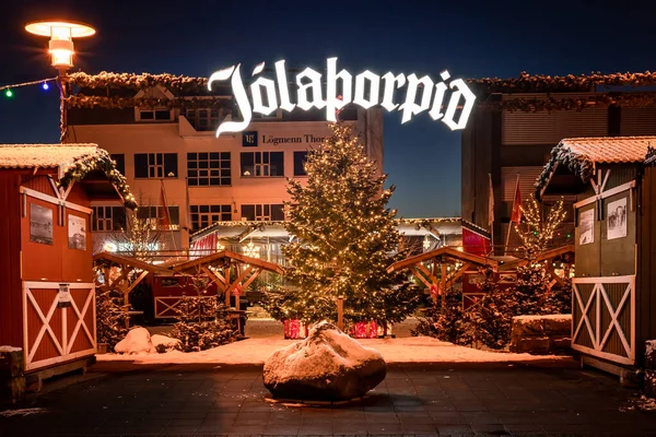 Hafnarfjordur, İzlanda - 4 Aralık 2021: Noel Pazarı girişinde neon tabela. Işıklarla süslenmiş ve karla kaplı Noel ağacı. İnsan yok, gece vakti..