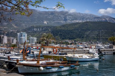 Budva, Montenegro - April 28, 2022: Small fishing boats moored at Budva harbour. Sunny day, hotel buildings and mountains in background.