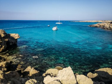 Deniz manzarası ve Blue Lagoon, Cape Greco, Kıbrıs kayalıkları. Küçük tekneler körfeze demir attı.. 