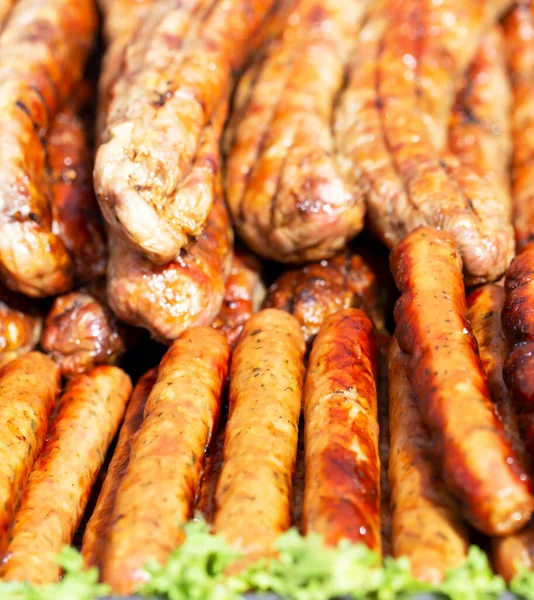 Fresh appetizing thick and thin fried sausages with greens lie on a plate in the sun. Food court, weekend and rest. Top view, close up