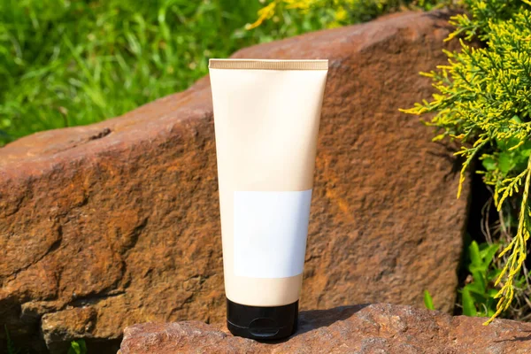 Beige cosmetic tube among stones and plants in the sun. Cosmetics, perfumes, beauty, fashion. Body cream, shampoo, hair conditioner, sunscreen, hand cream, lotion