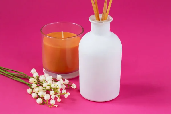 Ev için parfüm. Üzerinde vadi çiçekleri ve bir mum bulunan pembe bir zemin üzerinde Aromatik sazlık ayırıcı. Barış, rahatlama ve zevk kavramı