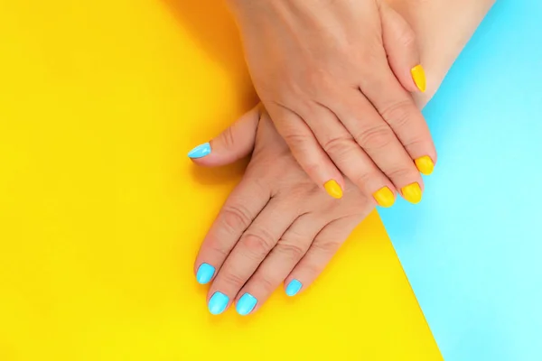 Manicured hands with light blue and yellow nails on yellow-blue background. Beauty and Fashion. Selective focus