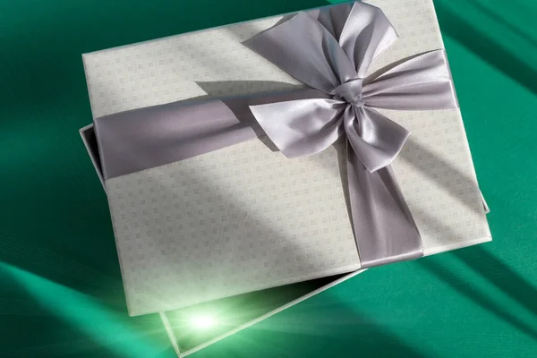 Gray festive slightly open gift box with bow on green background. Shining glow from the box. Birthday, wedding, Christmas, New Year and other holidays