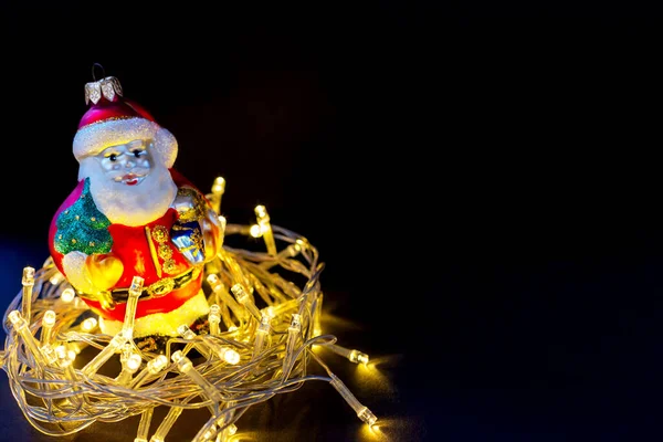 Toy Santa Claus in bright garland on dark background. New Year and Christmas background with copyright