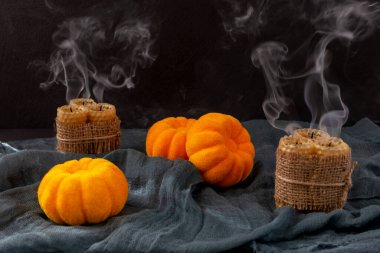 Cadılar Bayramı. Üç yapay balkabağı ve söndürülmüş mumlar, siyah bir arka planda, siyah bir kumaşın üzerinde uzanıyorlar.