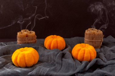 Cadılar Bayramı. Üç balkabağı ve söndürülmüş mumlar, onlardan gelen dumanla siyah bir arka planda siyah bir kumaş üzerinde uzanır.