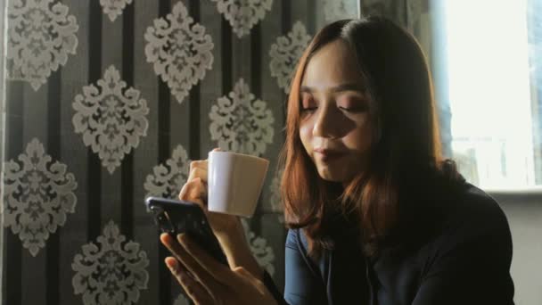 Avslappnad Vacker Asiatisk Kvinna Dricka Kaffe När Använder Mobiltelefon För — Stockvideo