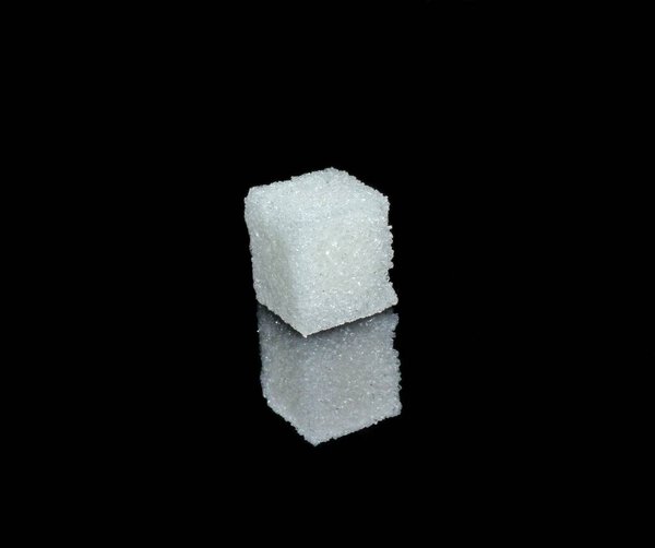 White sugar cube from crystals on black glossy glass 