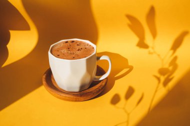 Sarı arka planda, yaprak gölgeli beyaz bir fincan kakao. Ön görünüm