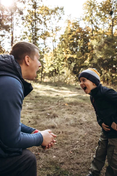 Gemeinsame Freizeit von Vater und Sohn. Der Vater sitzt auf einer Bank, und der Junge macht Grimassen — Stockfoto