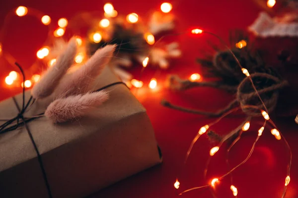 Ajándék díszített száraz lagurus piros alapon karácsonyi fények, közelkép — Stock Fotó