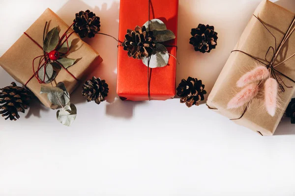 Presentes são decorados com pinho chique e flores secas em um fundo branco. Presentes são embalados em papel vermelho e bege — Fotografia de Stock