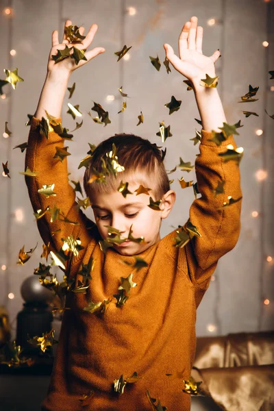 O menino joga fora o confetti dourado na forma de estrelas — Fotografia de Stock
