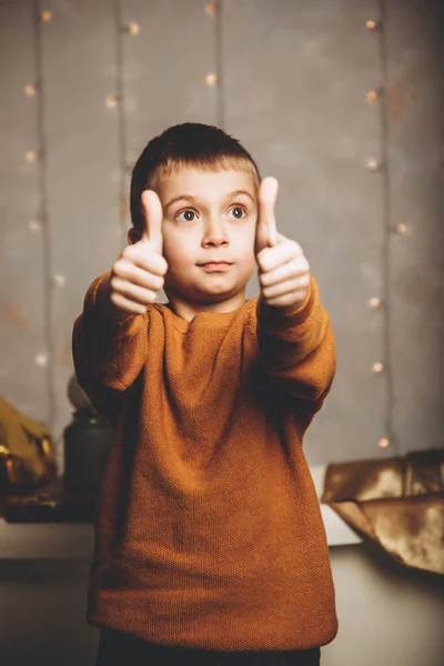 Menino de escola com uma camisola amarela a mostrar classe, super. Rapaz no fundo das luzes de Natal. Retrato de uma criança — Fotografia de Stock