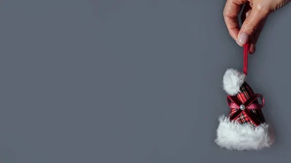 Різдвяна декоративна іграшка у вигляді Санта-капелюха в руці на сірому фоні. Банер — стокове фото
