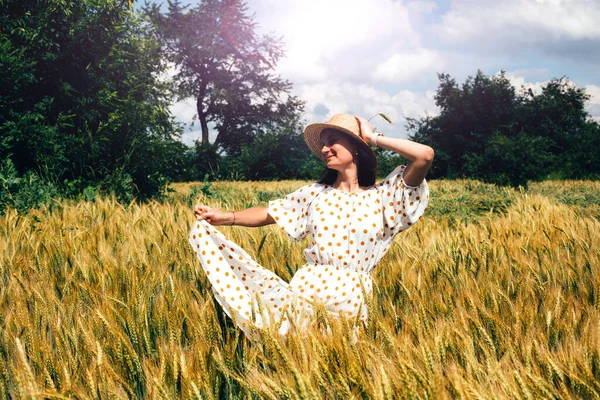 Das Mädchen im Weizenfeld trägt ein helles Kleid mit Tupfen und einen Strohhut. Konzept Ukraine — Stockfoto