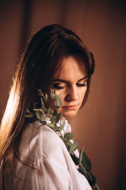 Güzel makyajlı bir kız elinde okaliptüs dallarıyla aşağıya bakıyor.