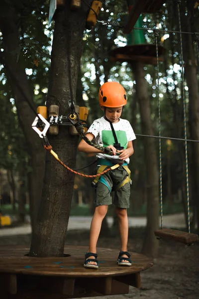 Un chico alegre en casco se divierte en el parque de cuerdas en verano — Foto de Stock