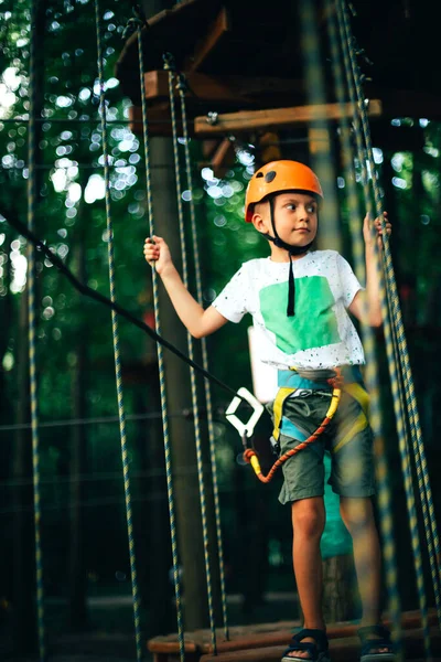 Kasklı neşeli çocuk gün batımında ip parkında eğleniyor.