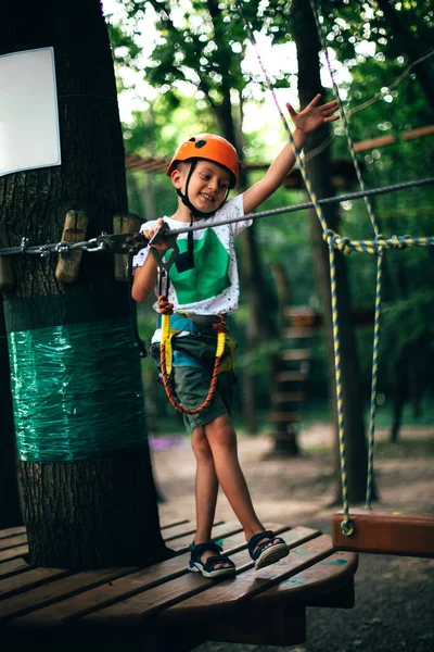 Chico alegre en un casco en verano divirtiéndose en un parque de cuerdas — Foto de Stock