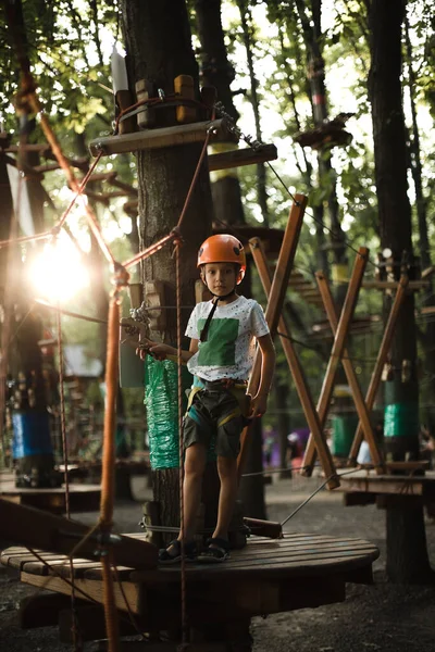 A cheerful boy in helmet has fun in the rope park at sunset in summer — Foto de Stock