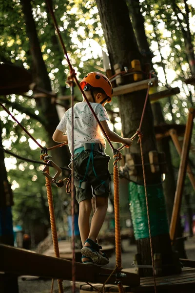 A cheerful boy in an orange helmet has fun in the rope park — Foto de Stock