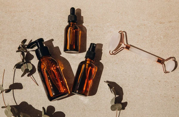 Flat lay, amber clear bottles with cosmetics and a facial roller on a light background — Stock Photo, Image