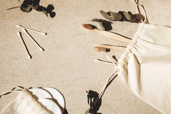 İki ahşap diş fırçası, pamuk yastık ve sopalar ve okaliptüs dallı hafif bir arka planda ahşap bir saç fırçası.