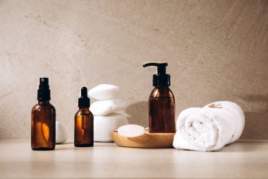 Üzerinde su damlaları olan şişeler tahta bir tabakta yüz silindiri ve bej arka planda beyaz taşlı bir havlu.