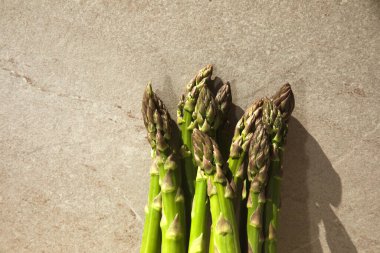 Taze, çiğ, yeşil kuşkonmaz bej taştan bir masada, gölgeli.