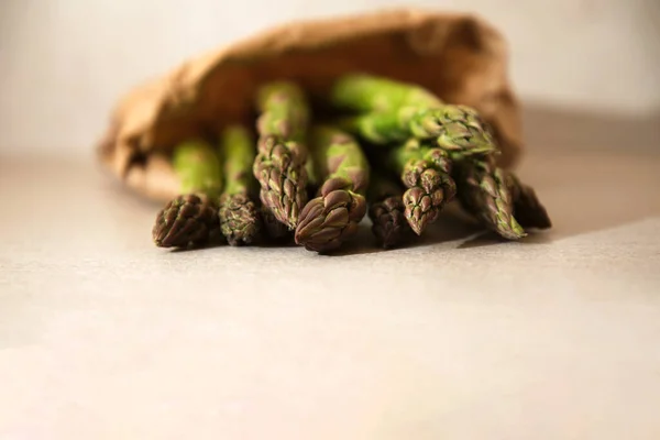 Espargos verdes frescos maduros em um saco de papel em uma mesa bege close-up, foco seletivo — Fotografia de Stock