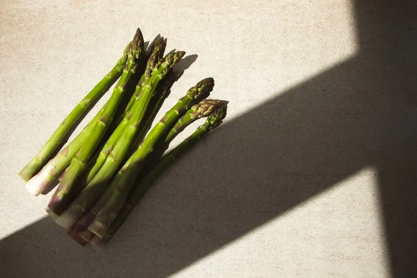 Frischer, roher, grüner Spargel auf beigem Steintisch und Fensterschatten — Stockfoto