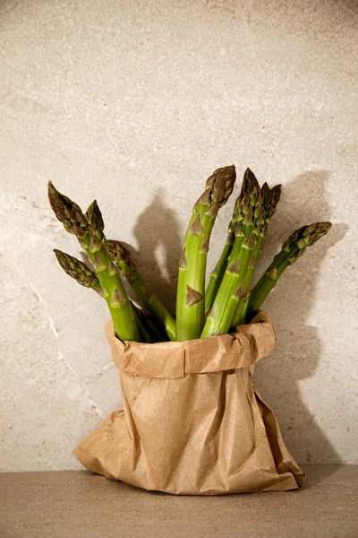 Ripe fresh asparagus in a paper bag on a beige table, front view