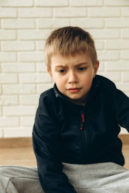 6-7 yaşlarında sinirli bir çocuk duvarın yanında oturuyor. Bir çocuğun portresi, ön manzara.