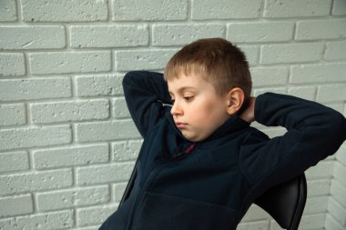 6-7 yaşlarında düşünceli bir çocuk balkonda bir sandalyeye oturup pencereden dışarı bakar. Bir çocuğun portresi.