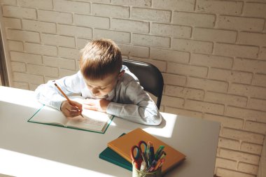 Bir öğrenci beyaz bir masadaki deftere numaralar yazıyor. Okul konseptine dönelim.