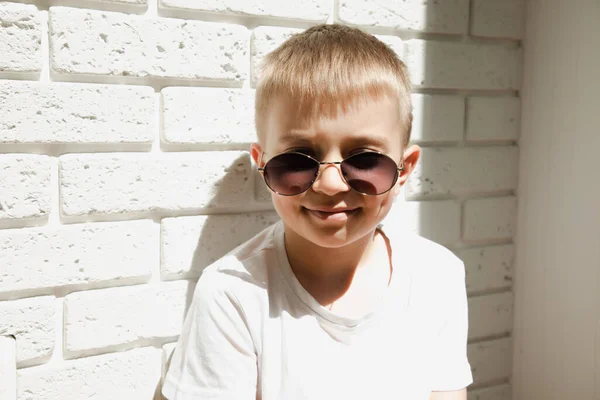 Menino Óculos Sol Senta Encostado Uma Parede Tijolos Sorri Retrato — Fotografia de Stock