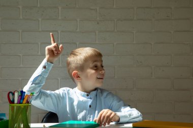 Beyaz bir masada oturan bir öğrenci bir fikri olduğuna dair el hareketi gösteriyor. Okul kavramı