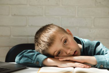 Çocuk online öğrenmekten bıktığı için masaya uzanır. Masadaki bir çocuğun portresi.