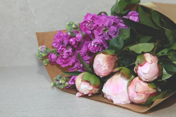 Bouquet of pink peonies and matthiola in craft packaging on a beige table, background. Front view