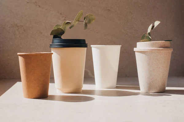 A set of cups made of eco-materials with eucalyptus branches. Disposable and reusable eco cups on a stone beige background. Front view