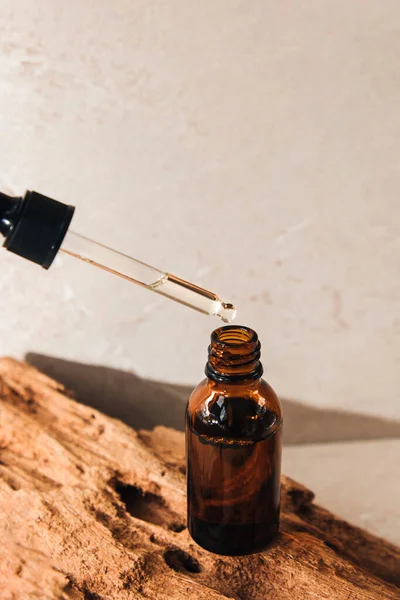 Open amber bottle of serum close-up on wooden podium. Glass boutique with a dropper