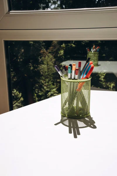 White office table with office supplies, colored pencils in green glass. Front view